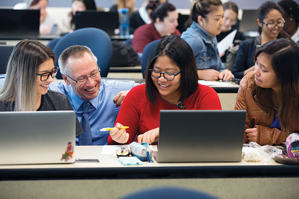 A SAIT instructor assists a student at a computer in a lab.