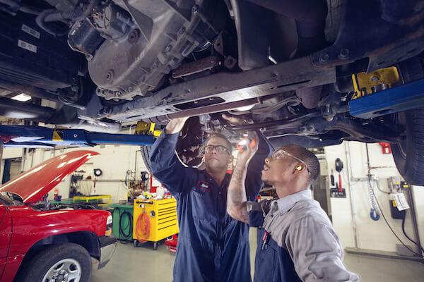 Two people looking at a car on a jack