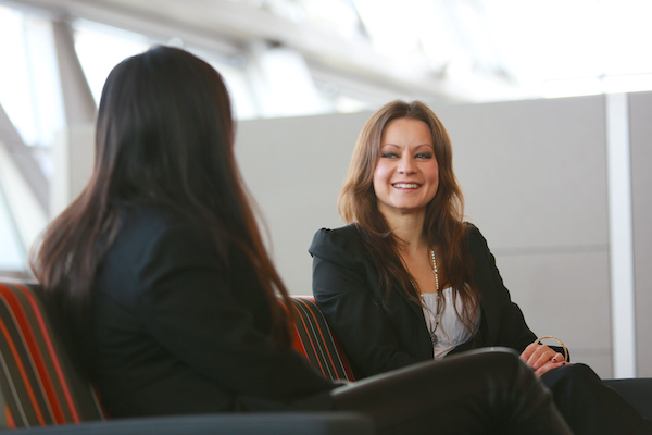 Two women wearing blazers sit and talk
