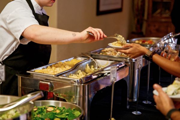 A person serving food from a buffet while another individual holds a plate.