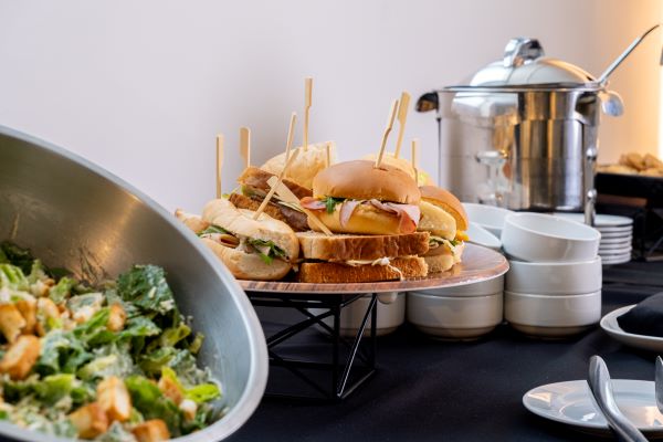 A display of assorted sandwiches on a platter alongside a bowl of Caesar salad at a buffet setting.