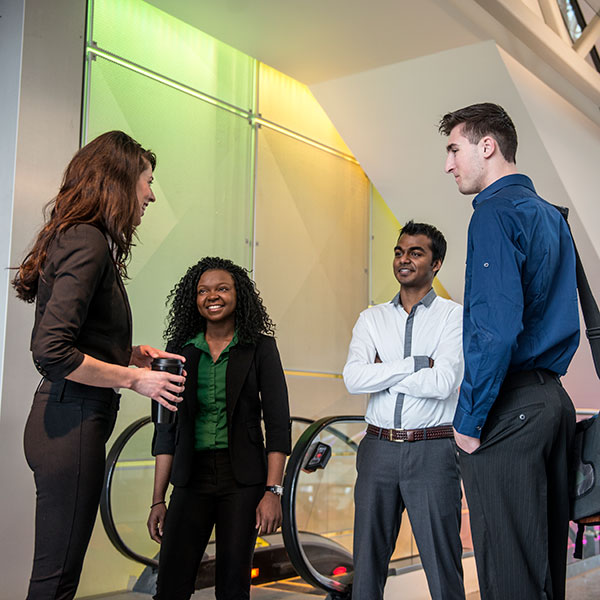 A group of professional speak around the bottom of an escalator within the Aldred Centre on SAIT campus.