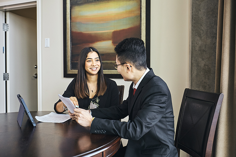 Two Hospitality and Tourism Management students wearing business attire speak at a table.