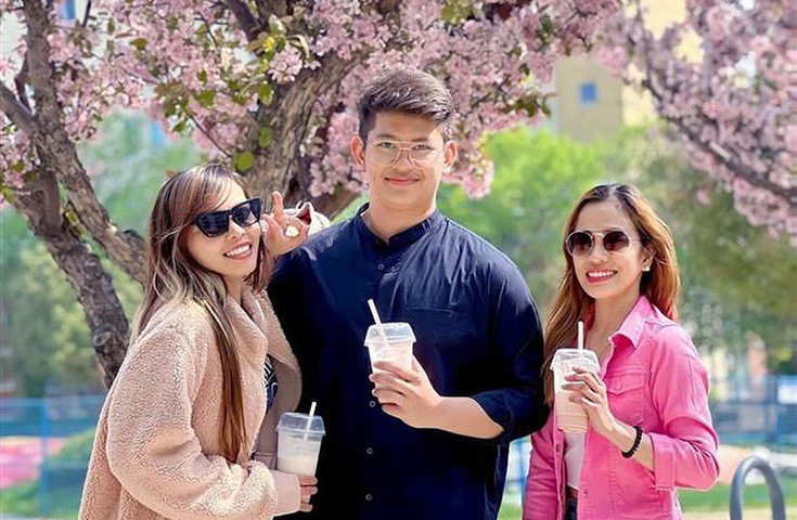 Three people stand in front of a tree with cherry blossoms holding iced coffee drinks.
