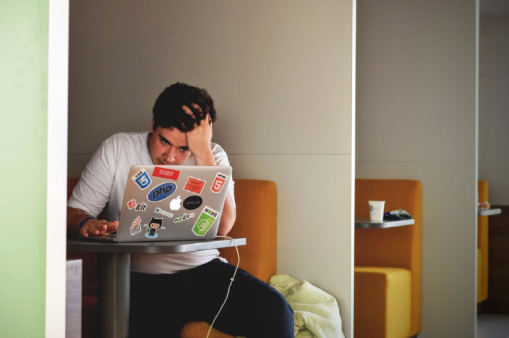 A student sits at a table looking at their laptop.