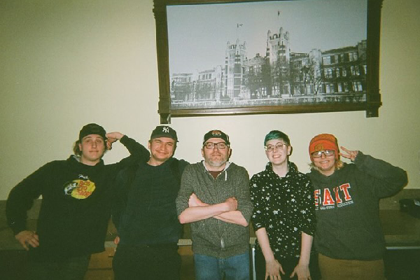 Five SAIT students stand in front of a vintage photograph of Heritage Hall.