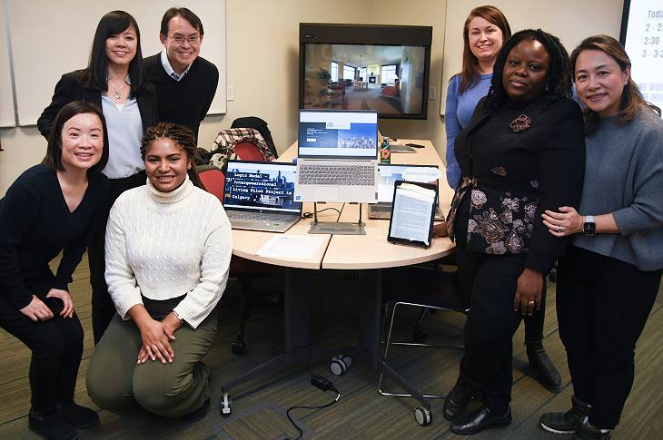 Seven students pose around a table looking at the camera. On the table, there are three laptops showing report content (illegible).