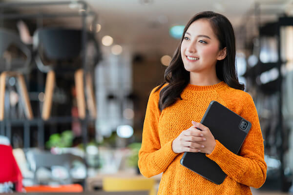 A woman holding a tablet to her chest smiling
